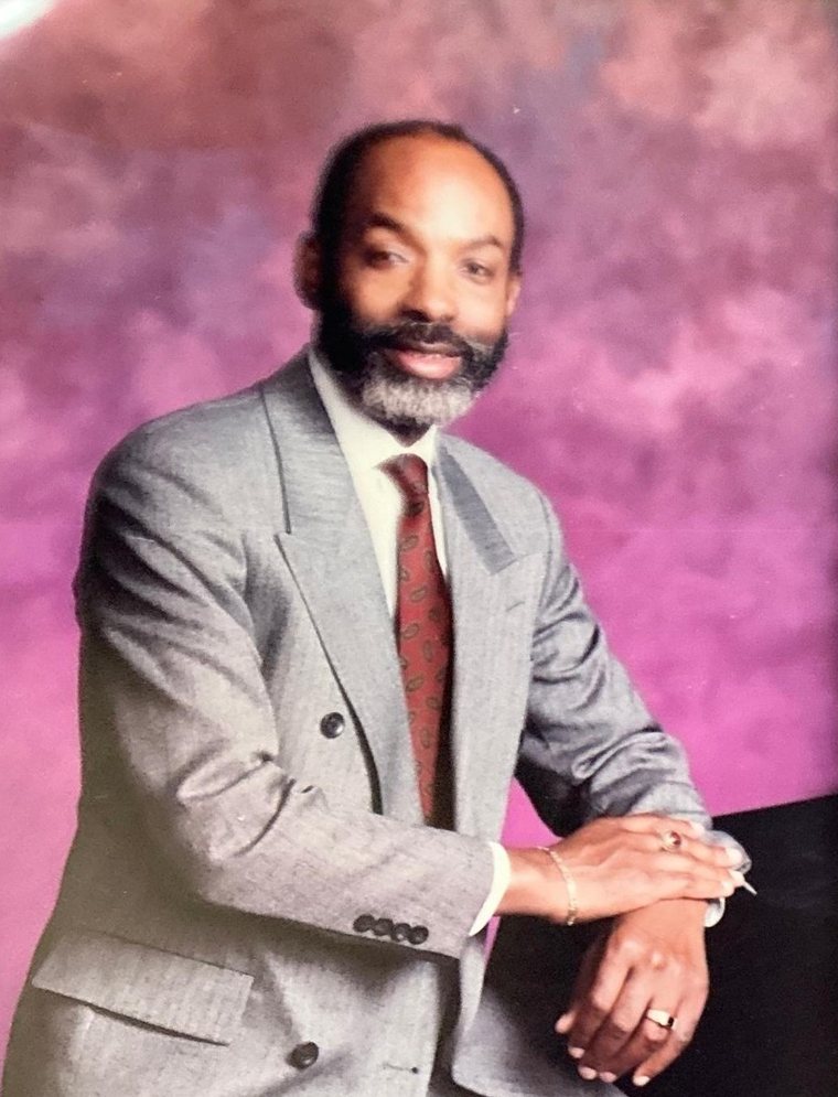 Studio portrait of Leon Collier in a grey suit and red patterned tie.